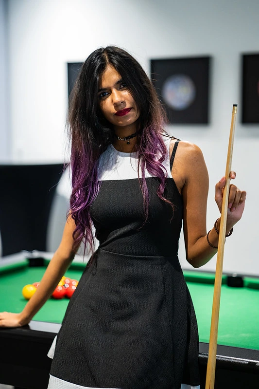 une belle femme cougard qui tiens une queue assise sur un billard