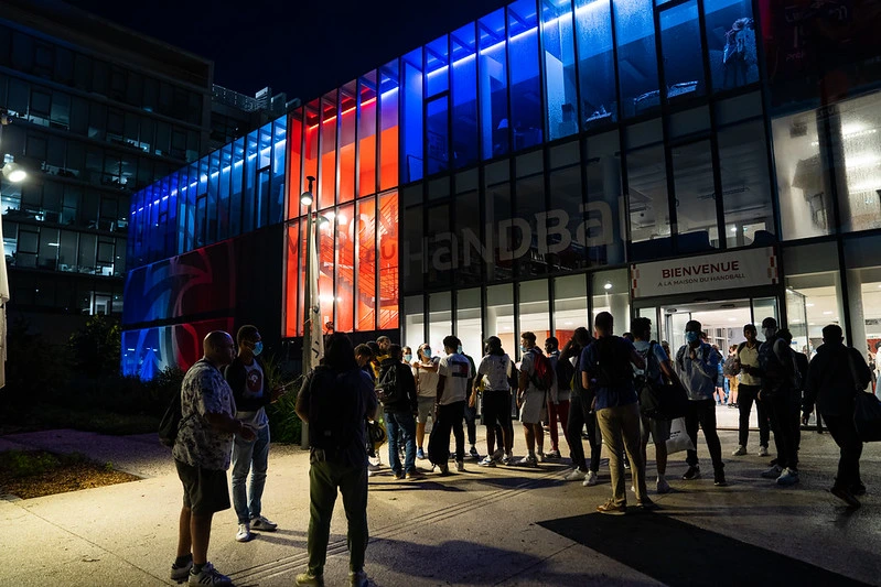 des joueurs devant la maison du handball éclairé par les lumières la nuit