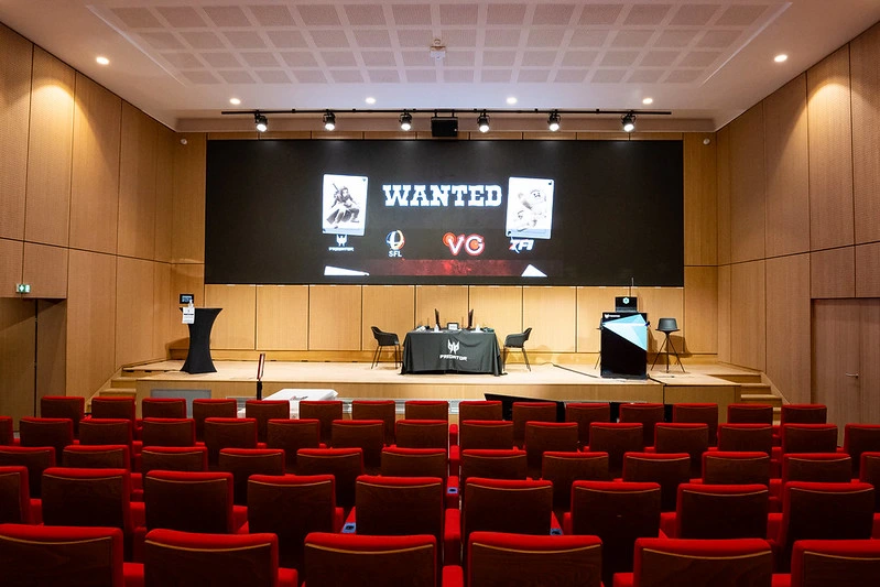 auditorium de la maison du handball avec un écran allumé et WANTED affiché et une salle vide